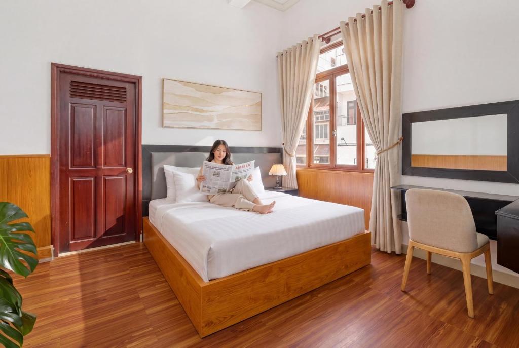 a woman sitting on a bed reading a newspaper at Eluna Lilly Da Lat Hotel in Da Lat