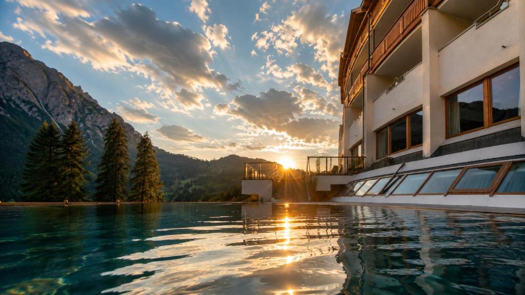 a hotel swimming pool with a sunset in the mountains at Hotel Asterbel in Braies