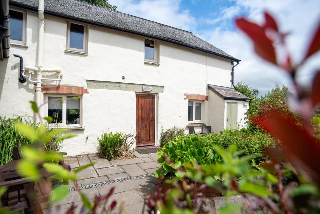 a white house with a wooden door in a yard at The Barn - Old Mill Cottages in Ilfracombe