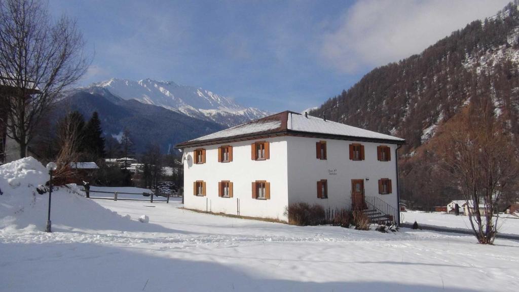 ein weißes Haus im Schnee mit Bergen im Hintergrund in der Unterkunft Chasa Randulina in Sta Maria Val Müstair