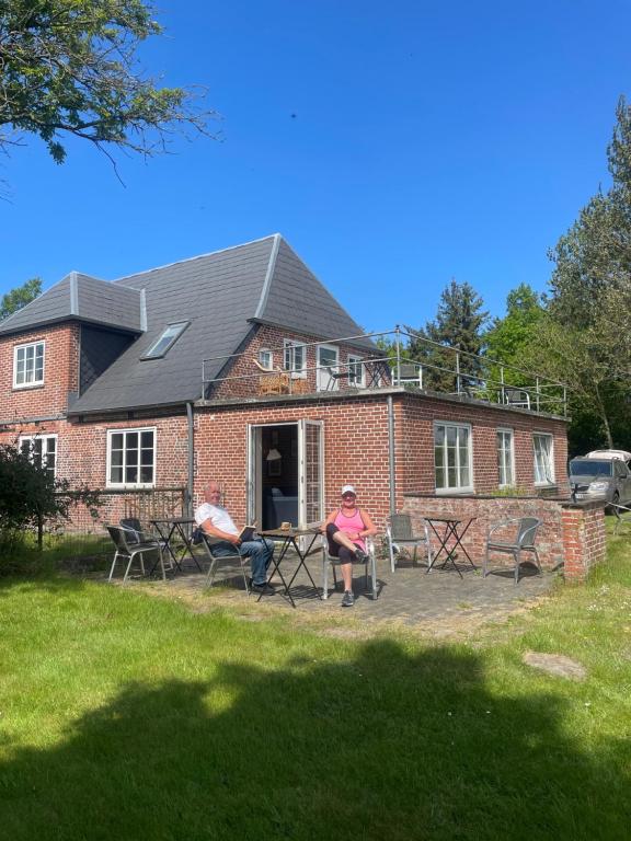 two people sitting at a table in front of a brick house at Hellesbnb in Rømø