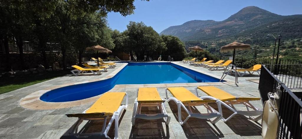 a swimming pool with yellow chairs and a bunch of tables at Casas Rurales Cortijos el Encinar in Torres