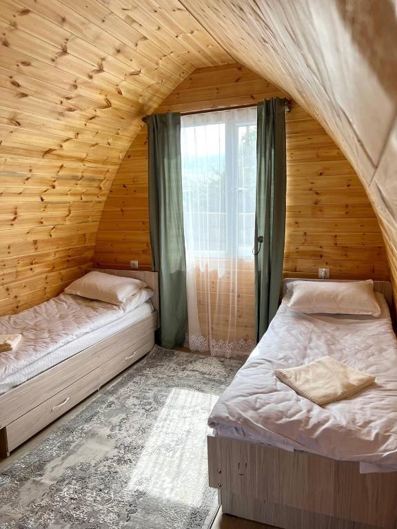 two beds in a wooden room with a window at Beshik Guest House in Bokonbayevo