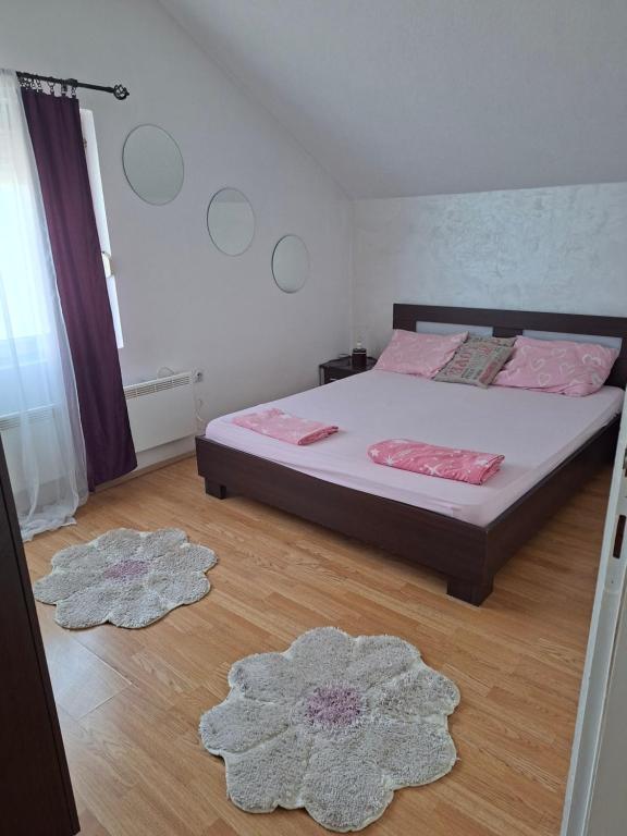 a bedroom with a bed with pink pillows and two rugs at Stan na dan -Bratunac- in Bratunac