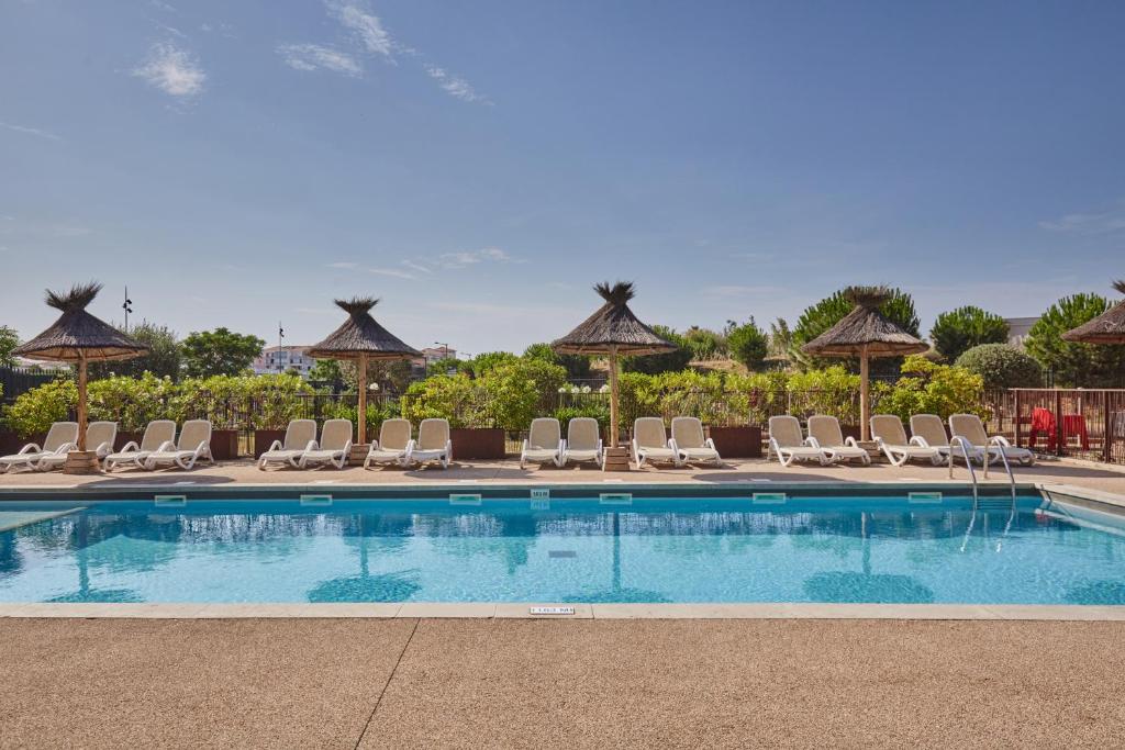 a swimming pool with chairs and umbrellas at Résidence Odalys Terra Gaia in Sète