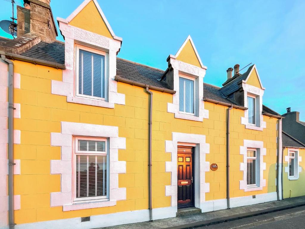 a yellow house with white trim on a street at Seaspray in Buckie