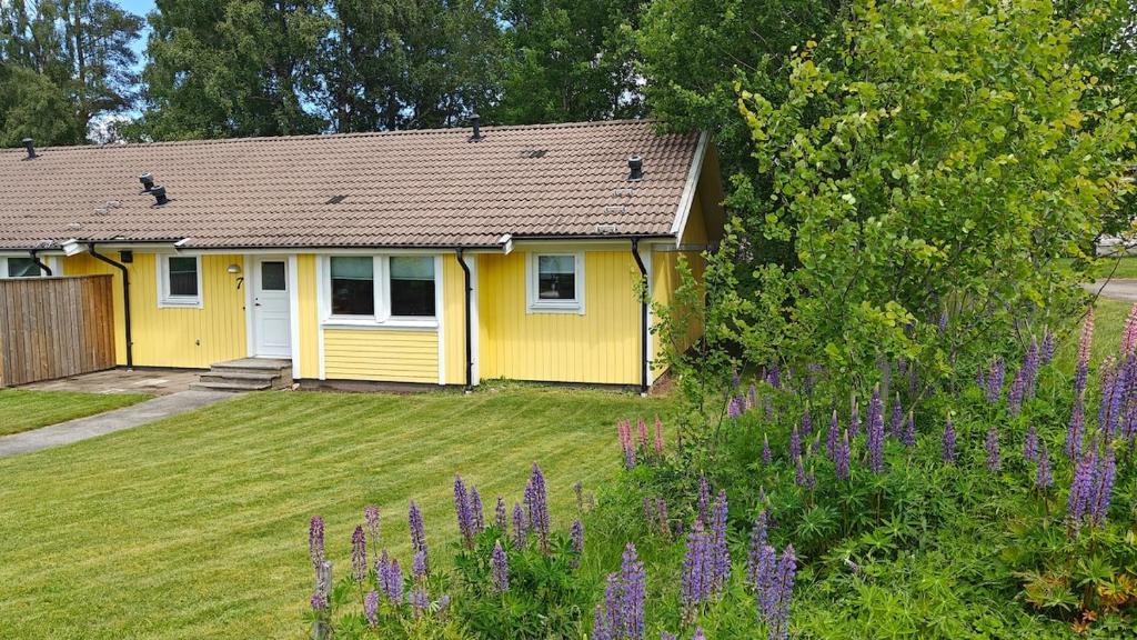 a yellow house with a yard with purple flowers at Gårdsjö 7 in Gårdsjö