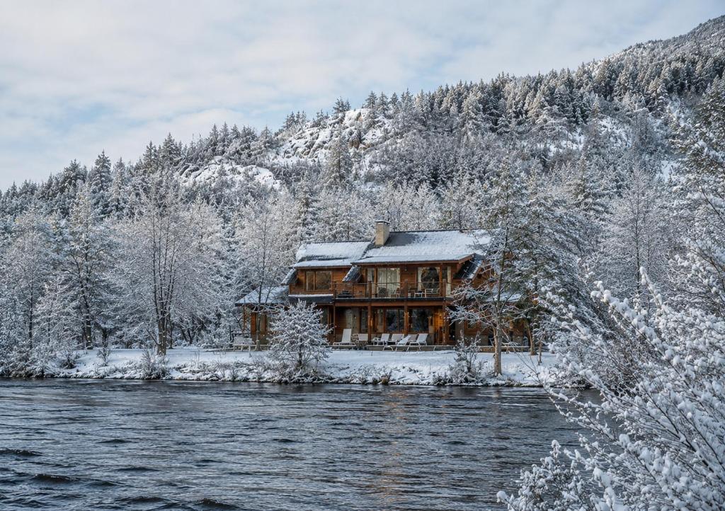 a log cabin in the snow next to a river at Rio Hermoso Hotel De Montaña in San Martín de los Andes