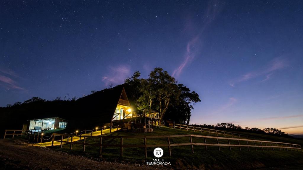 a house with a tree and a fence at night at Rancho Sol Poente - Rancho Queimado - SC in Rancho Queimado