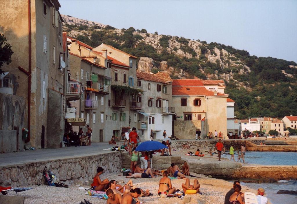a group of people sitting on the beach on the water at Apartment IVANKA -KROK in Baška