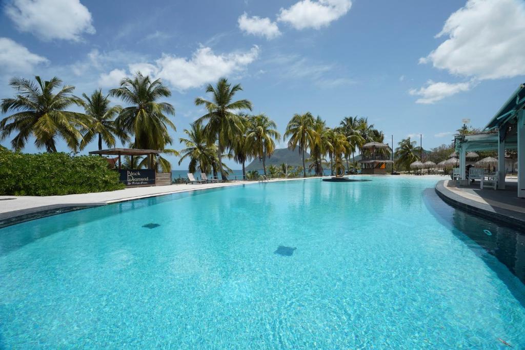 a large swimming pool with palm trees in the background at Suite Sabi Vue Mer in Le Diamant