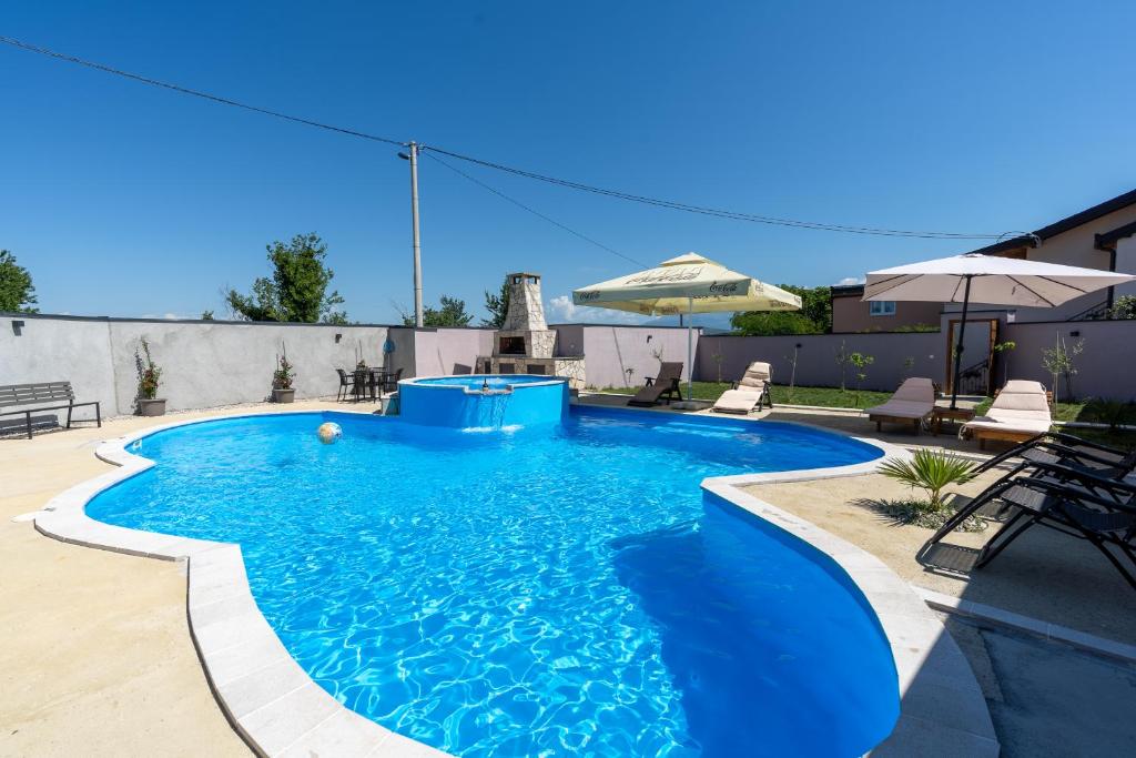 a blue swimming pool with chairs and an umbrella at Villa Bali Oasis Grand Wellness in Stolac