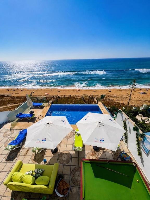 a pool with umbrellas and chairs and the beach at Maison Bella View in Moulay Bousselham