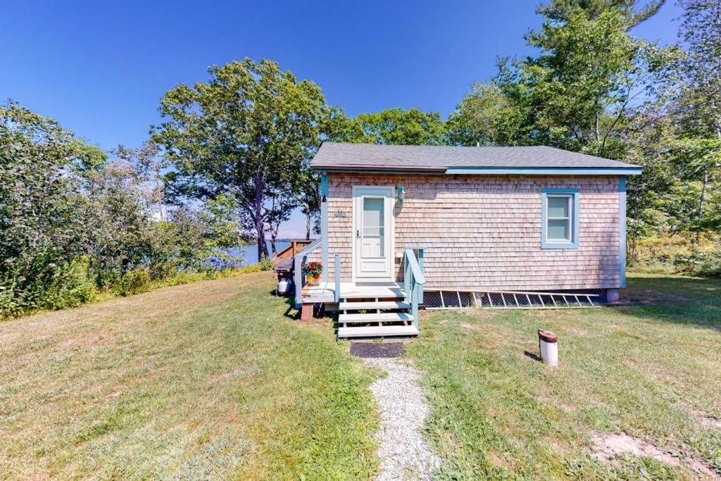 a small house on a grassy field with a porch at Waterfront home on St George River with private beach & deck - near festivals in Cushing