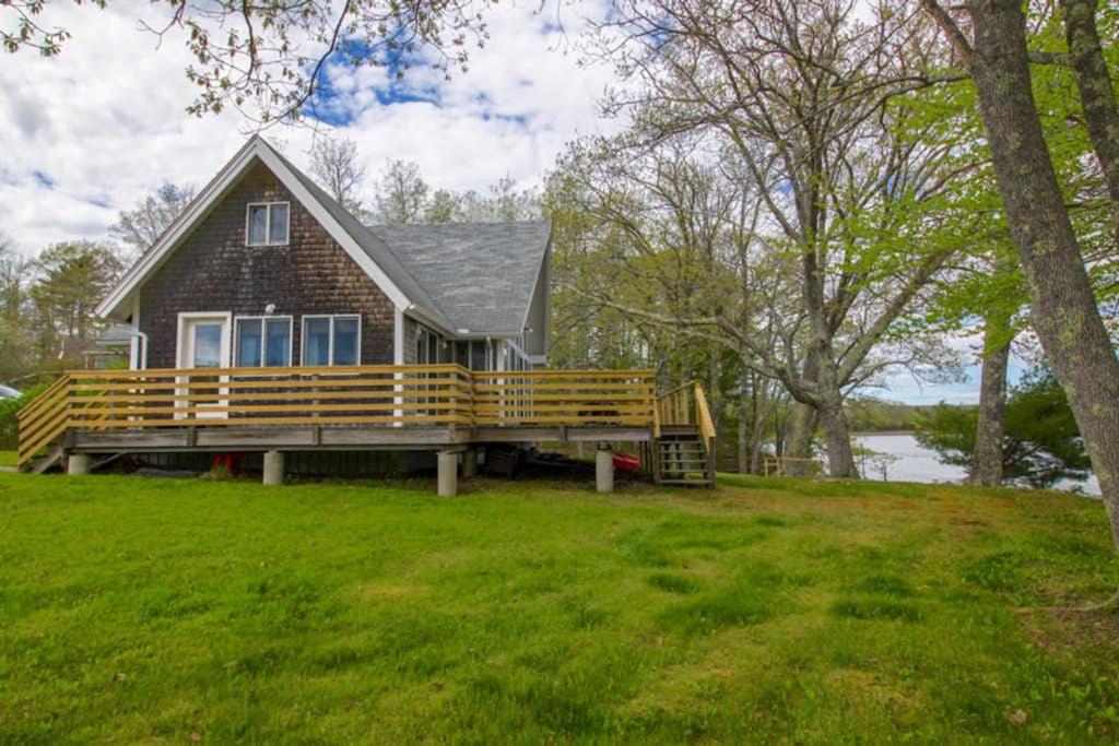 a house with a large deck on a grass field at Remodeled Waterfront Home with Wraparound Deck, Water Views, & Beach Access in Waldoboro