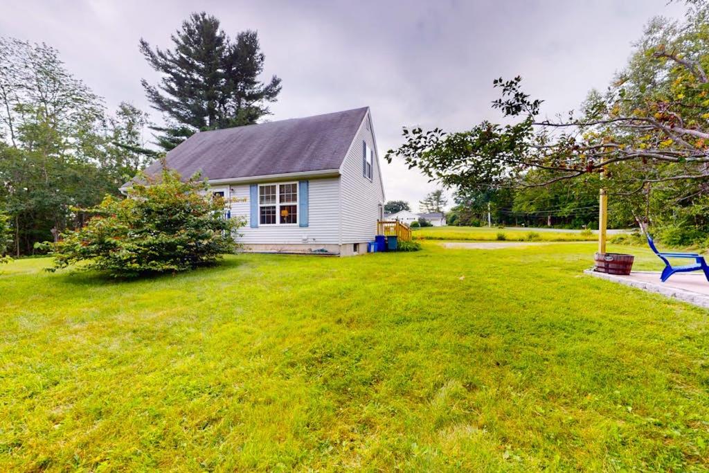 a small white house in a field of green grass at Serene home with a deck, grill, firepit, board games, washer/dryer, & mtn views in East Lamoine