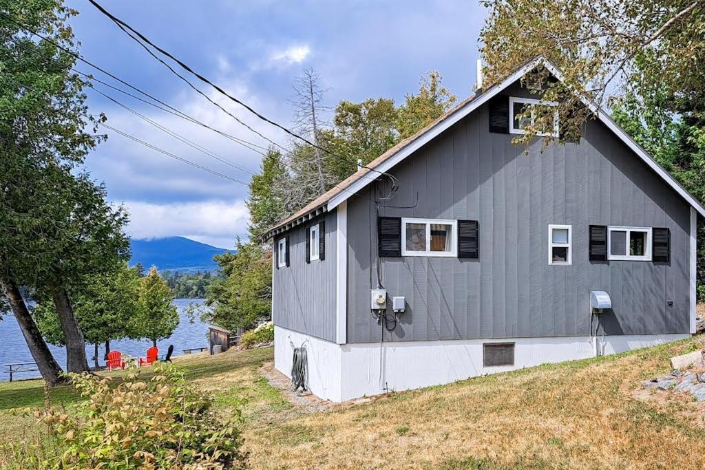 a gray house on a hill next to a body of water at Lakefront, cabin-inspired home with firepit, grill, & screened porch, Wifi in Greenville