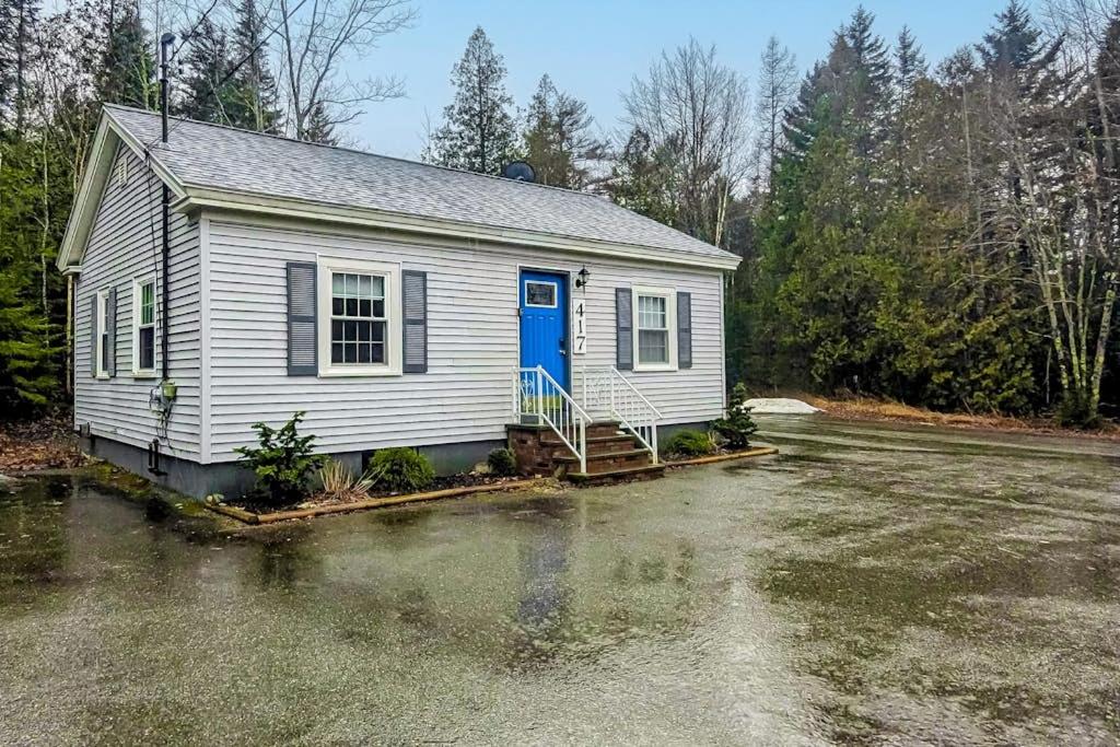 a small white house with a blue door on a lot at Open layout Maine cottage with washer/dryer & grill - dog-friendly in Gouldsboro