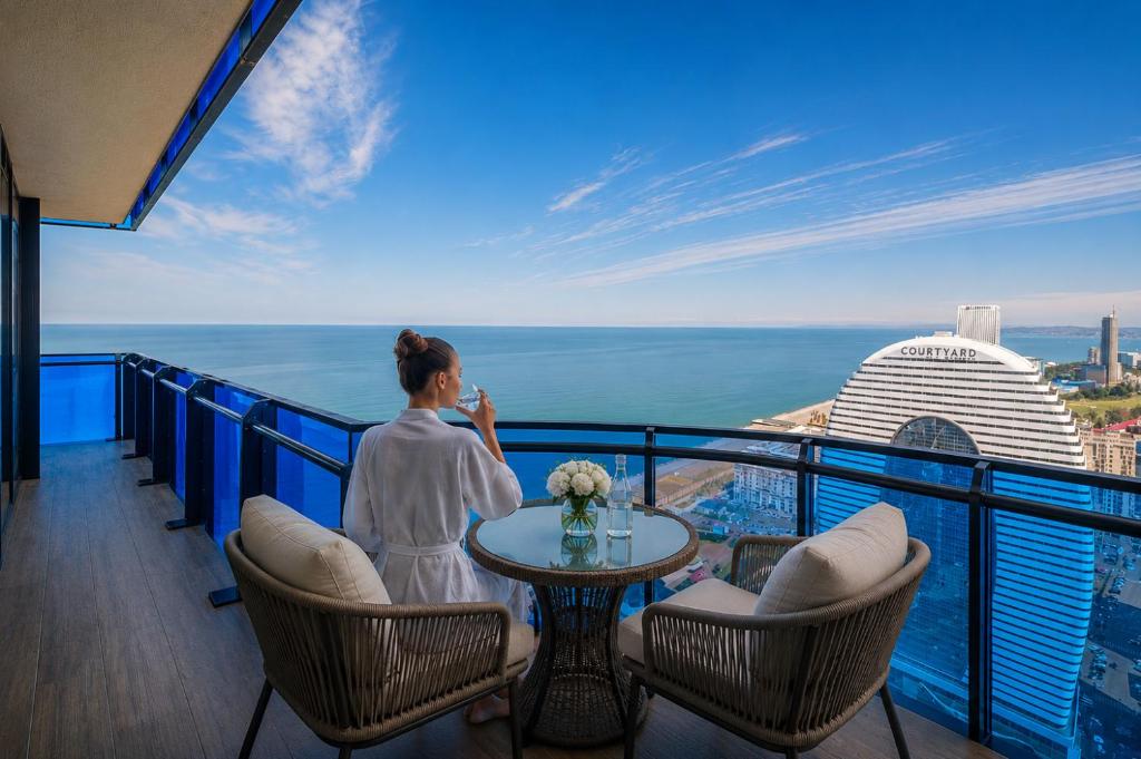 a woman standing on a balcony with a table and chairs at Royal Sea View Batumi in Batumi
