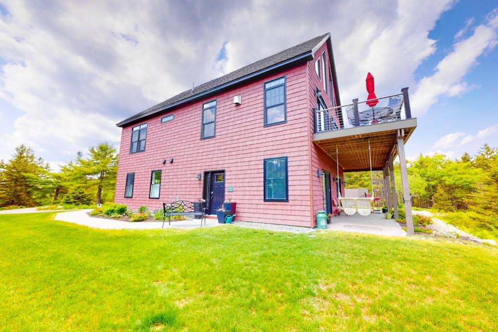 a red house with a balcony on top of a yard at Secluded hilltop home with beautiful Cadillac Mountain view and multiple decks in Bar Harbor