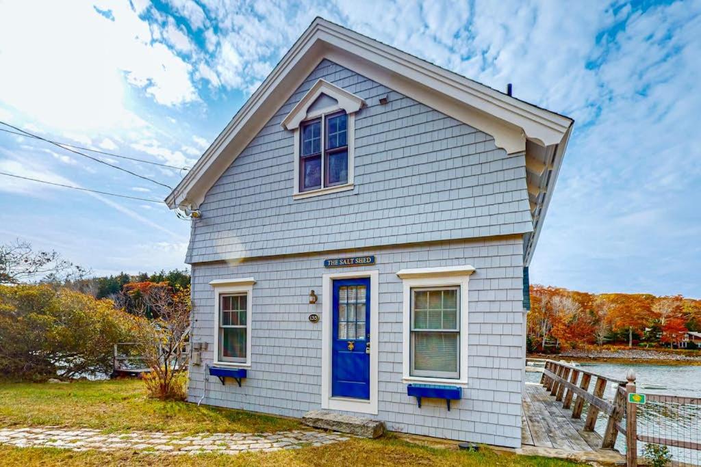 a small white house with a blue door at Enchanting Oceanfront Cottage with Breathtaking Views and Modern Comforts in East Boothbay