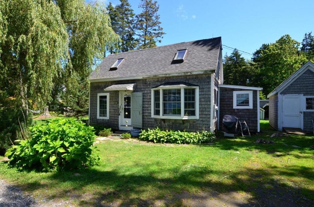 a small house with a green yard with a tree at Berry Cottage, private dock, overlooking a sandy b in South Thomaston