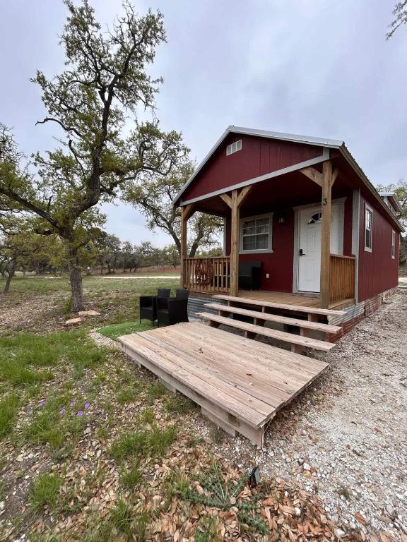 a red building with a deck in a field at Hill Country Cabin 3 in Canyon Lake