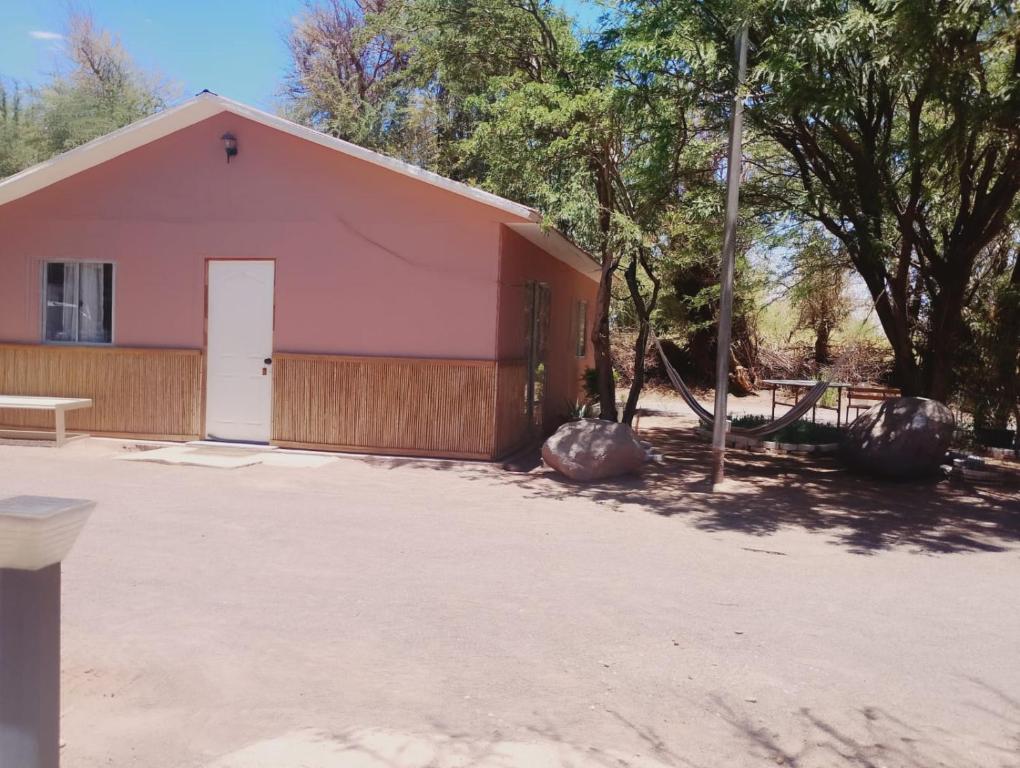 a pink building with a white door and trees at Cabañas rústico in San Pedro de Atacama