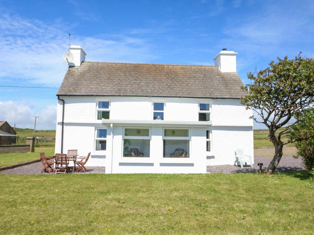 a white house with two chairs and a tree at Teach Feirme in Clonakilty