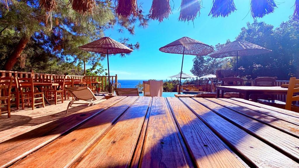 eine Holzterrasse mit Tischen, Stühlen und Sonnenschirmen in der Unterkunft Reflections Camp in Faralya