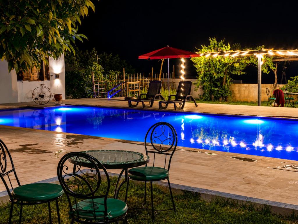 a table and chairs by a pool at night at Villa Mouloud - Piscine partagée, nature et calme in Khenifra