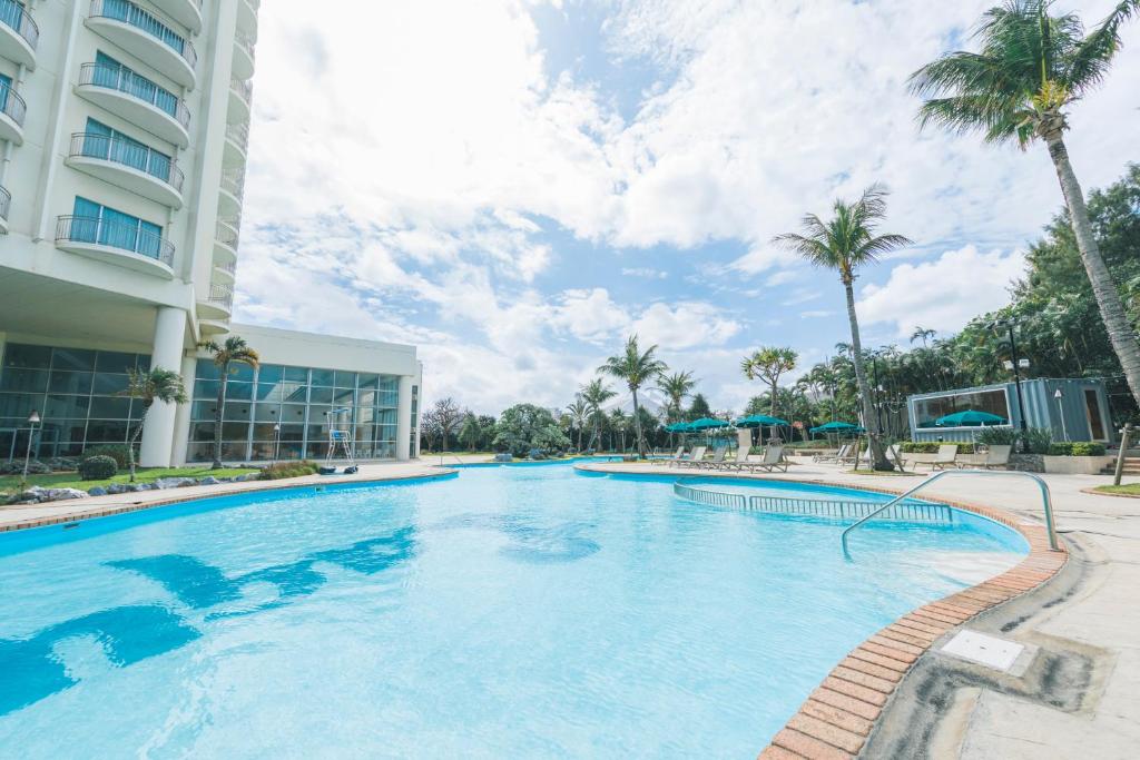 a large swimming pool in front of a building with palm trees at Laguna Garden Hotel in Ginowan