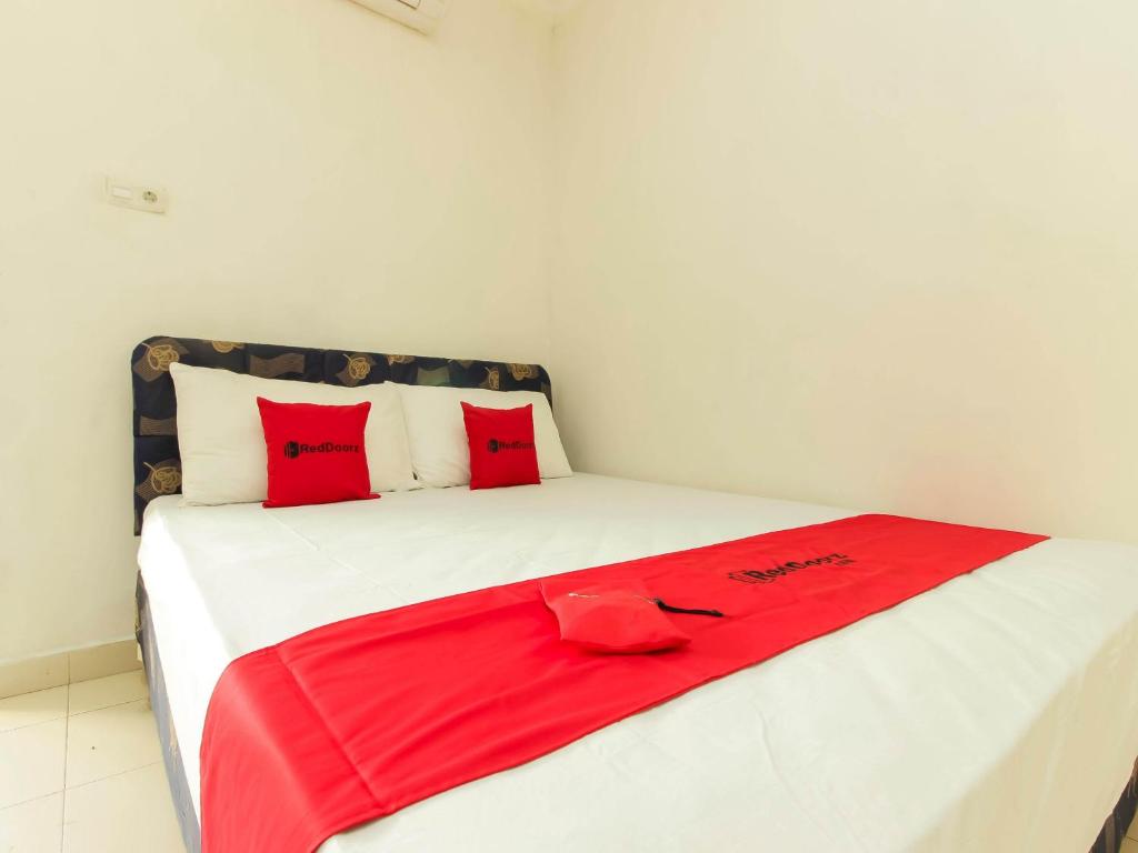 a white bed with red pillows and a red blanket at RedDoorz @ Malalayang Manado in Manado