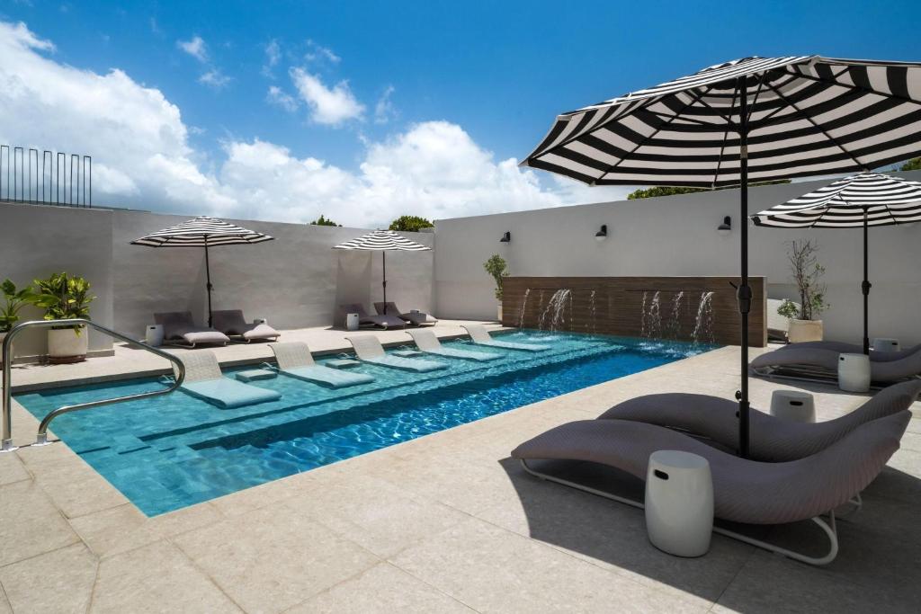 a swimming pool with chairs and umbrellas next to at Bali Hotel Adults Only Isla Verde, a Trademark by Wyndham in San Juan