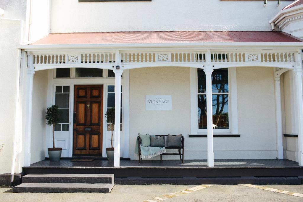 a front porch of a white house with a chair at The Vicarage Boutique Bed and Breakfast Oamaru in Oamaru