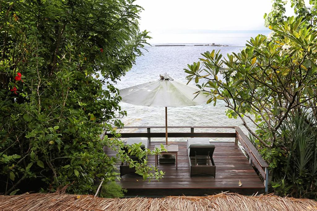 eine Holzterrasse mit einem Sonnenschirm und Stühlen auf dem Wasser in der Unterkunft Pondok Pisang Candidasa in Candidasa