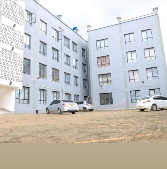 two cars parked in front of a large building at EMIC Suites in Nyahururu