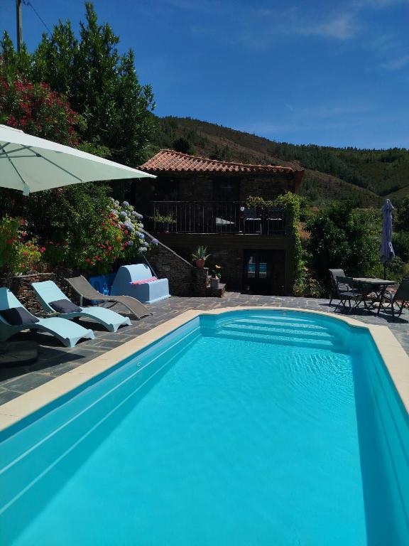 a blue swimming pool with chairs and a house at Bela Vista Alqueve - traditional stone house and private pool in Arganil