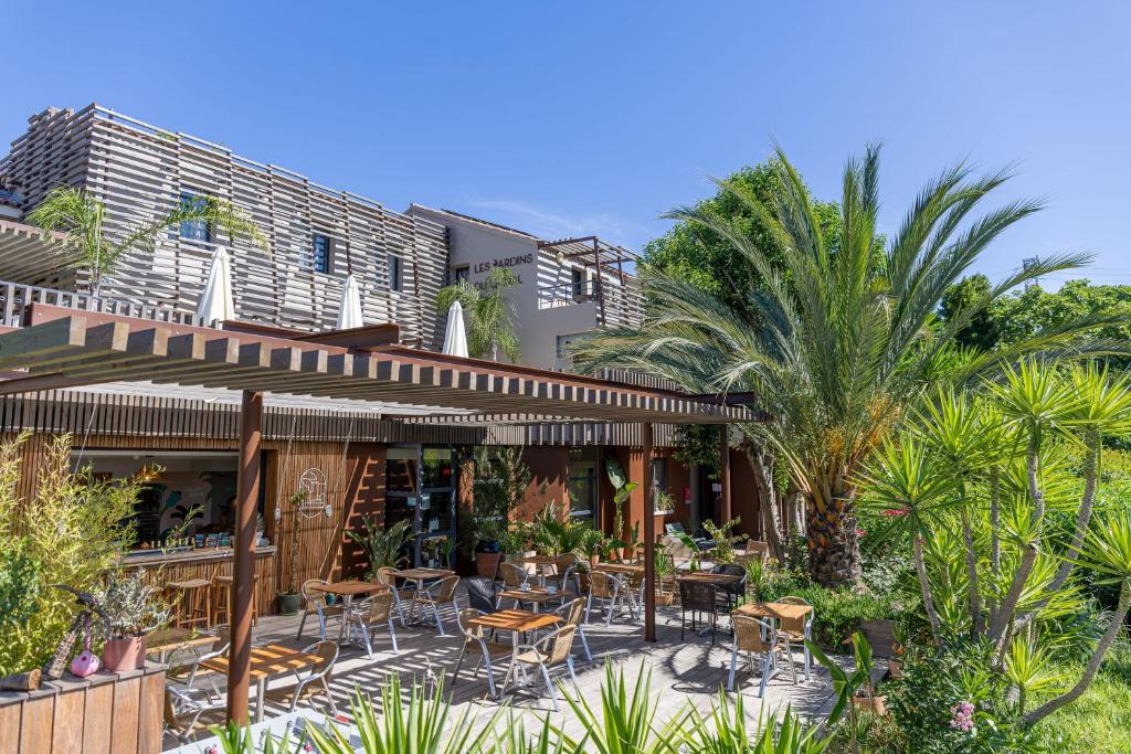 a patio with tables and chairs and palm trees at Hôtel les jardins du canal - piscine chauffée - solaire eco responsable - parking - garage - bornes électriques - accueil vélos - kids friendly in Aigues-Mortes