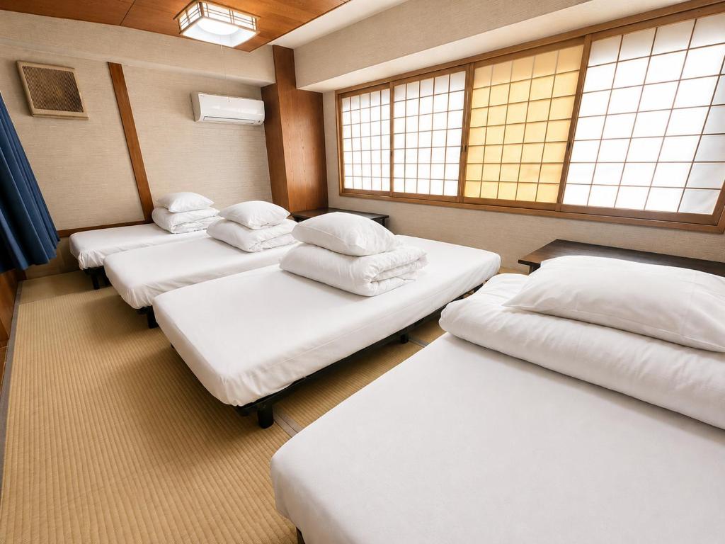 four beds in a room with windows in a room at Osaka Guesthouse Sakura in Osaka