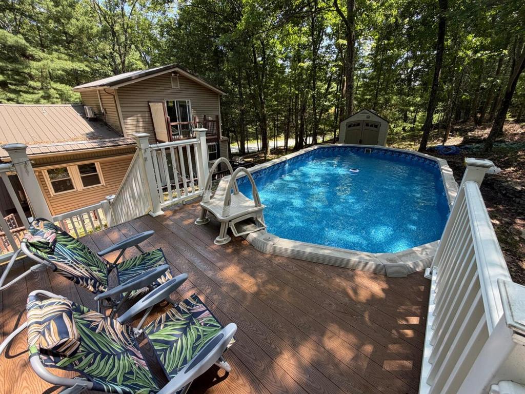 a pool on a deck with chairs and a house at Poconos Hideaway in Greentown