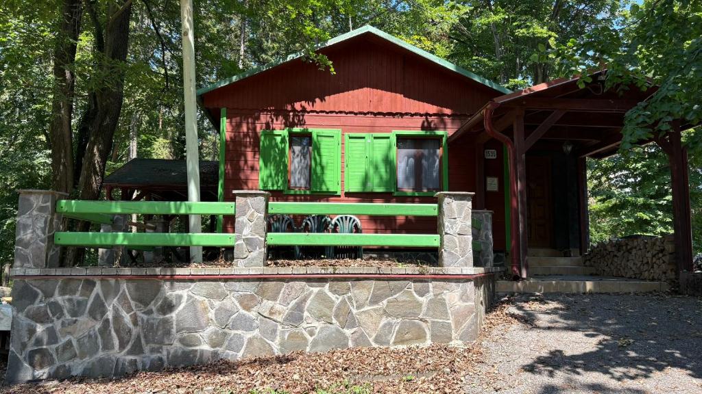 a small red and green house with a stone wall at Chata U malého Janka in Bojnice