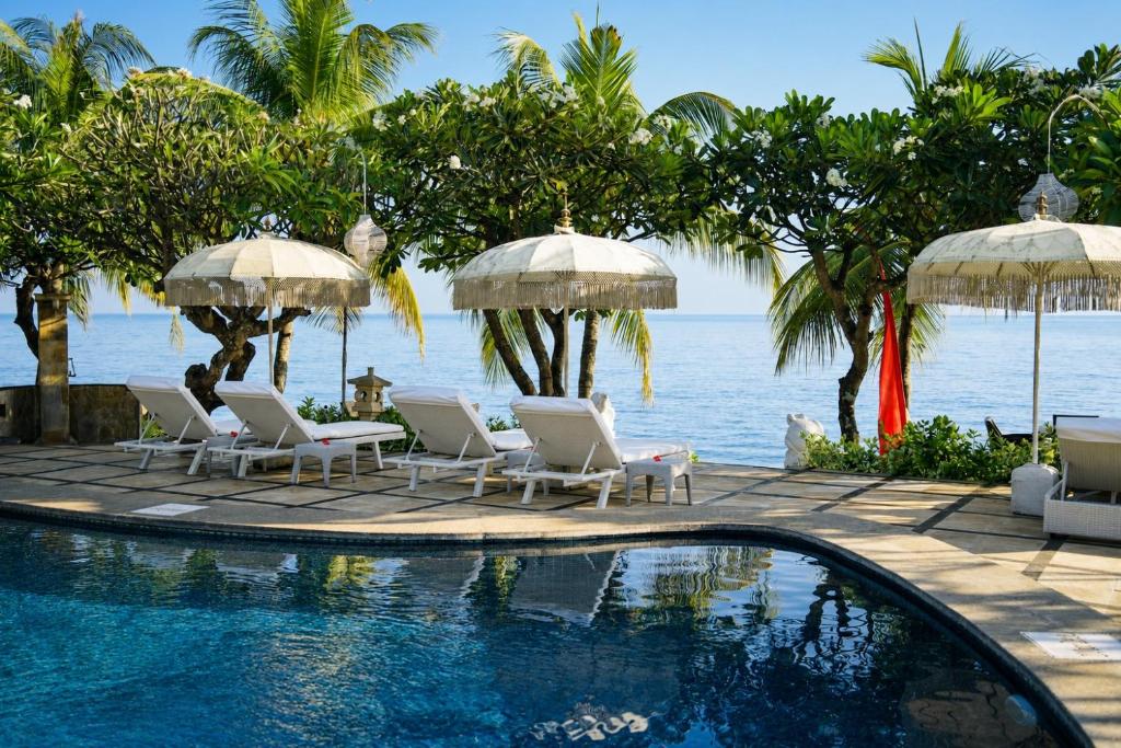 a swimming pool with chairs and umbrellas next to the ocean at Poinciana Resort in Tejakula