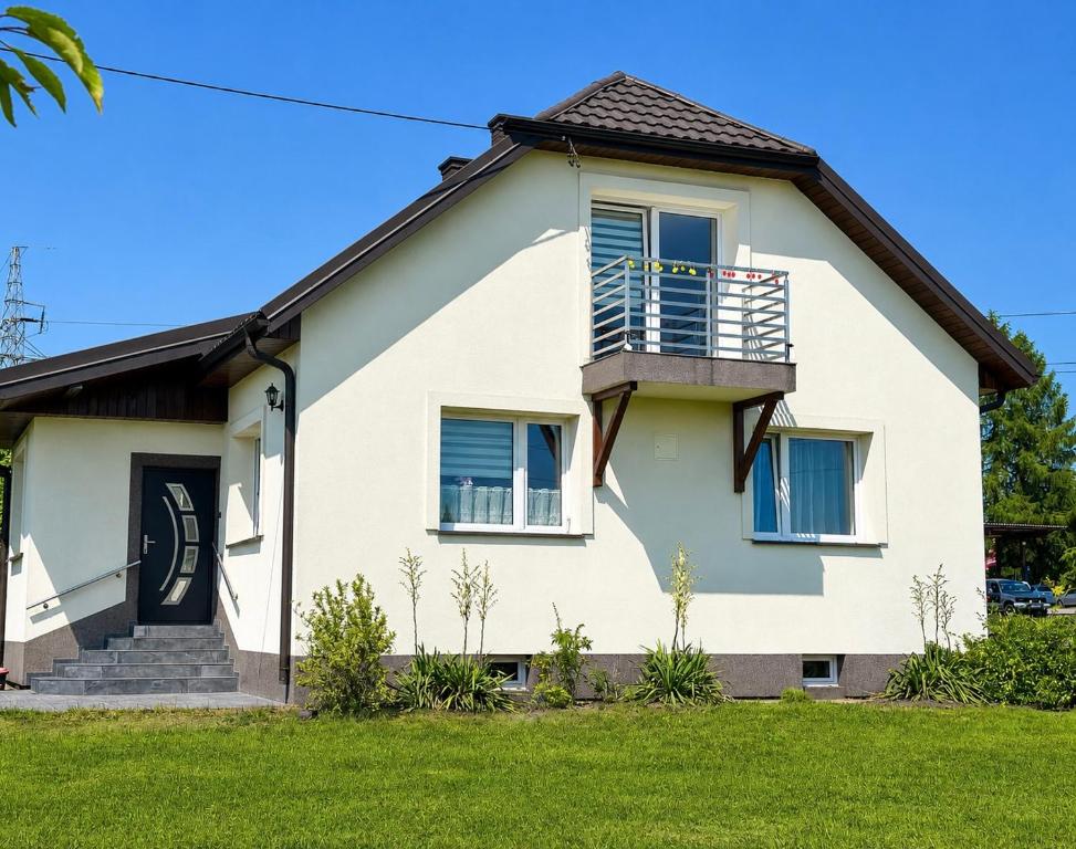 a white house with a balcony and grass at Aura Poręba Żegoty in Poręba Żegoty