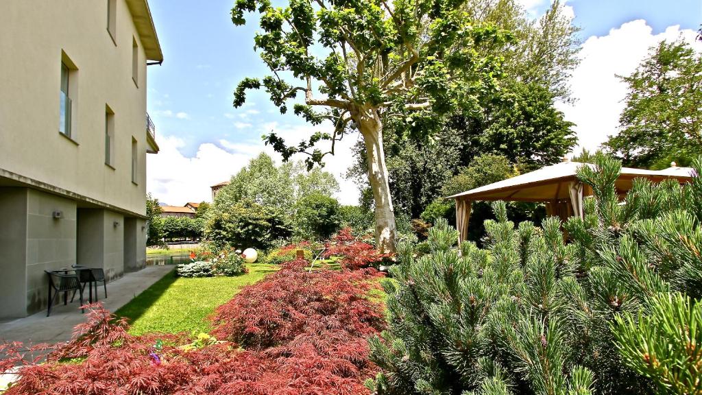 un jardin avec des plantes et un arbre ainsi qu'un bâtiment dans l'établissement Hotel La Sosta, à Cisano Bergamasco