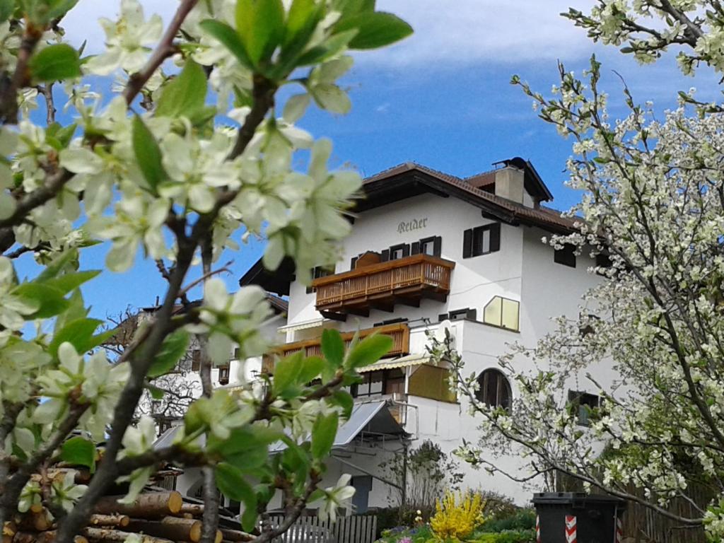 a white building with a balcony and trees at Garni Reider in Meltina