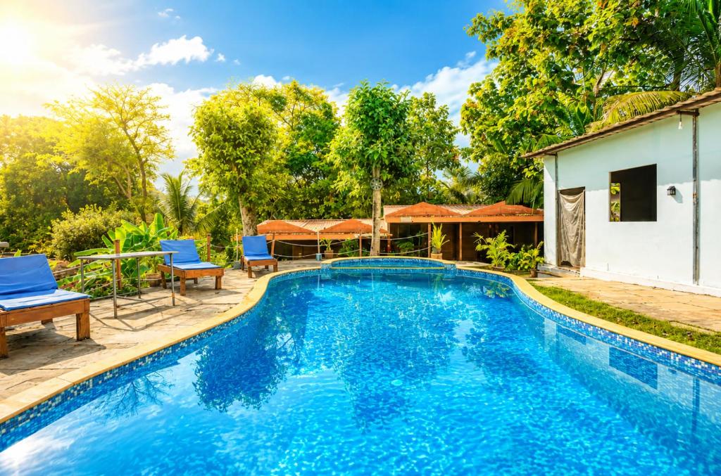 a swimming pool with blue chairs and a house at Royalstar Resort in Vagator