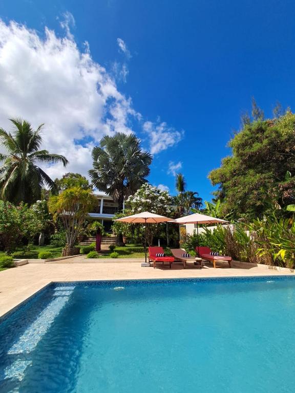 a swimming pool with chairs and umbrellas in front of a house at Maison Orita in Nosy Be