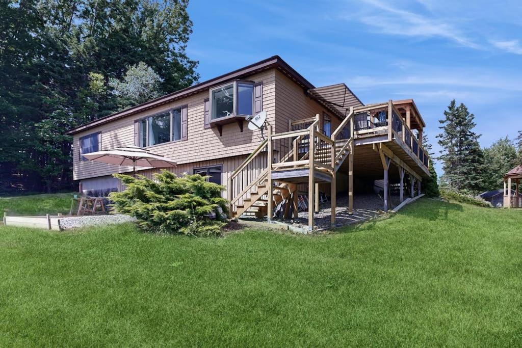 a large house with a deck on a green lawn at Charming Lakefront House with Outdoor Firepit, Washer/Dryer and Wifi in Gouldsboro