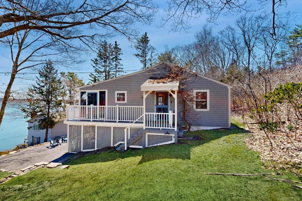 a small house on the side of a body of water at Dog-friendly river-view home with wood stove, deck, patio, dock, beach, grill in Boothbay